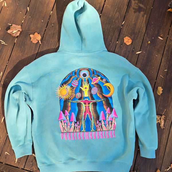 Light blue hoodie with colorful graphic design on a wooden surface with leaves.